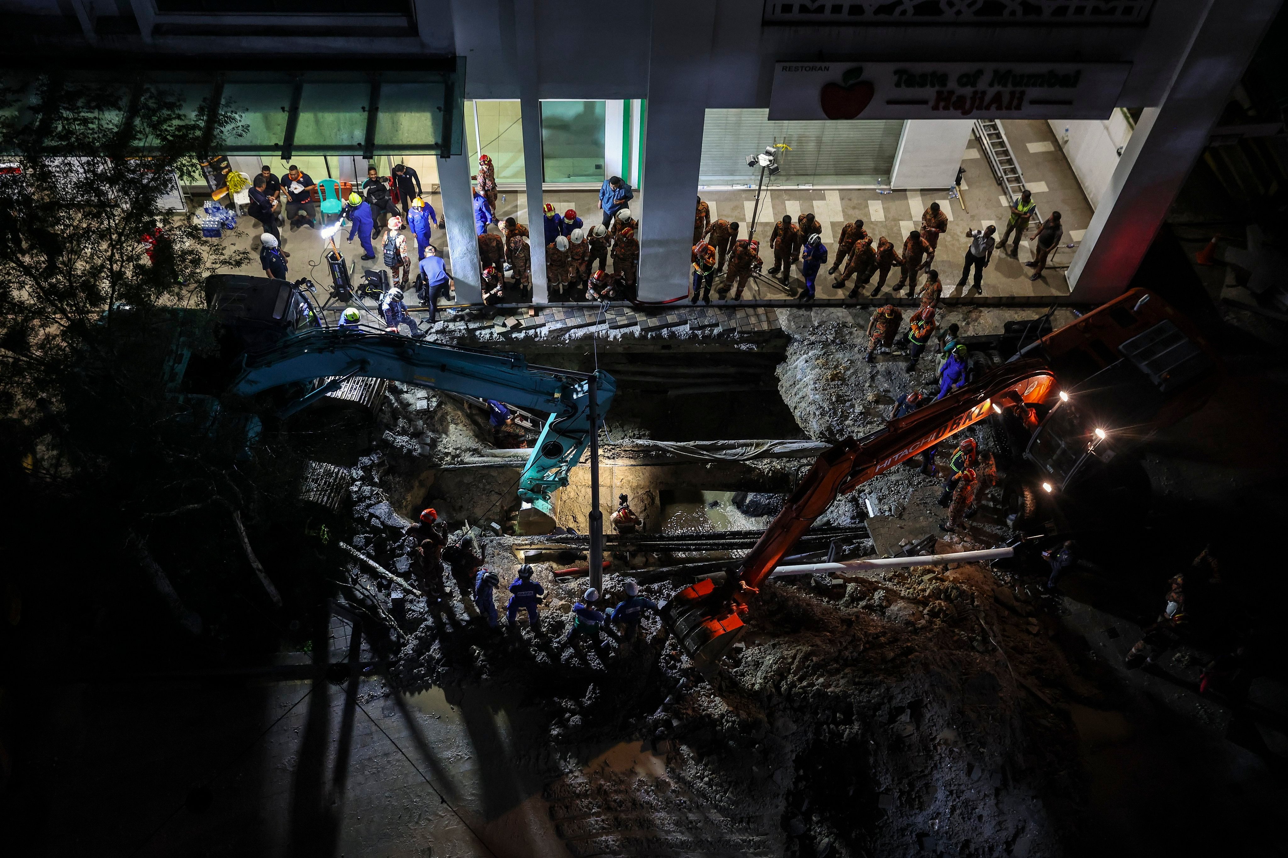 Rescuers inspect the site where a woman fell into the sinkhole in Kuala Lumpur on Friday. Photo: EPA-EFE